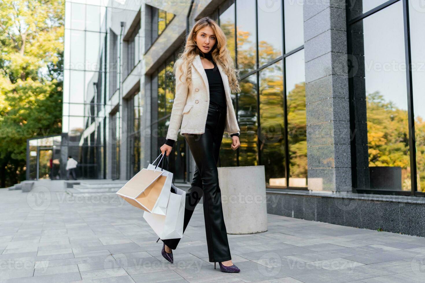 Shopping and fashion concept. Elegant blond woman in casual trendy outfit walking over modern shopping center with  paper bags.  Full lenght. photo