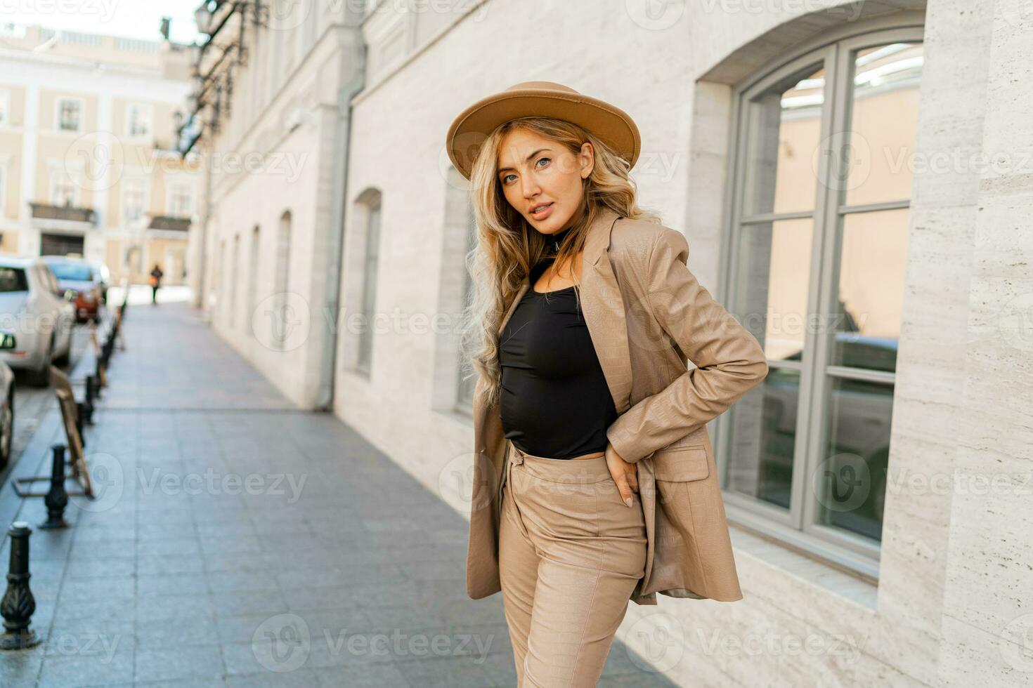 Fashion outdoor photo of stylish blond woman with perfect wavy hairs in beige hat and casual suit.