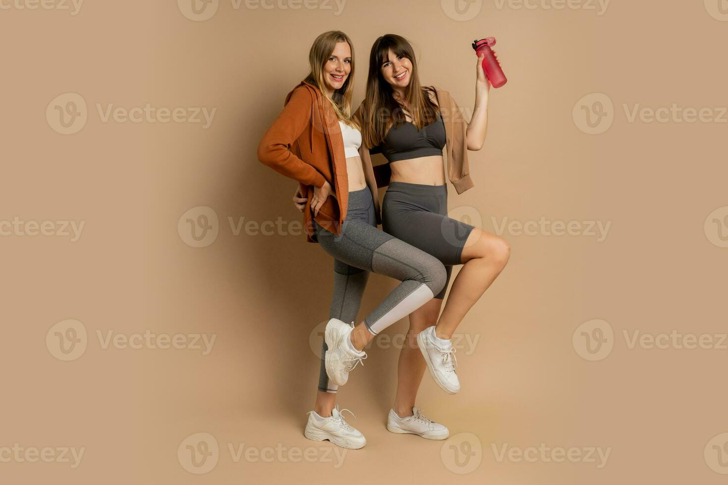Two sportive women in stylish fitness cwear posing  on beige background. Healthy lifestyle concept. Full lenght. photo
