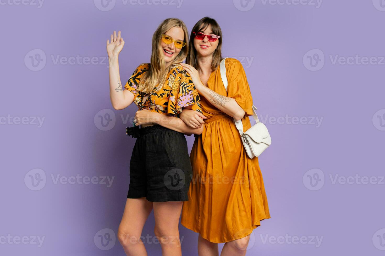 Two pretty women , best friends, posing on purple background in trendy  summer outfit. photo