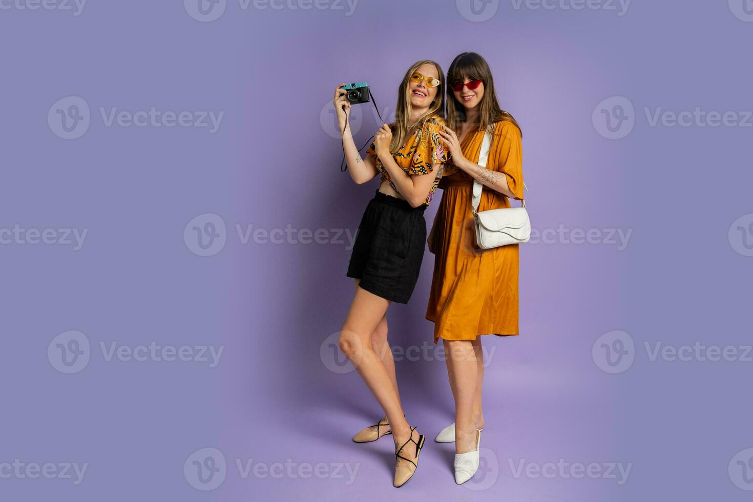 Two pretty women , best friends, posing on purple background in trendy  summer outfit. Full lenght. photo