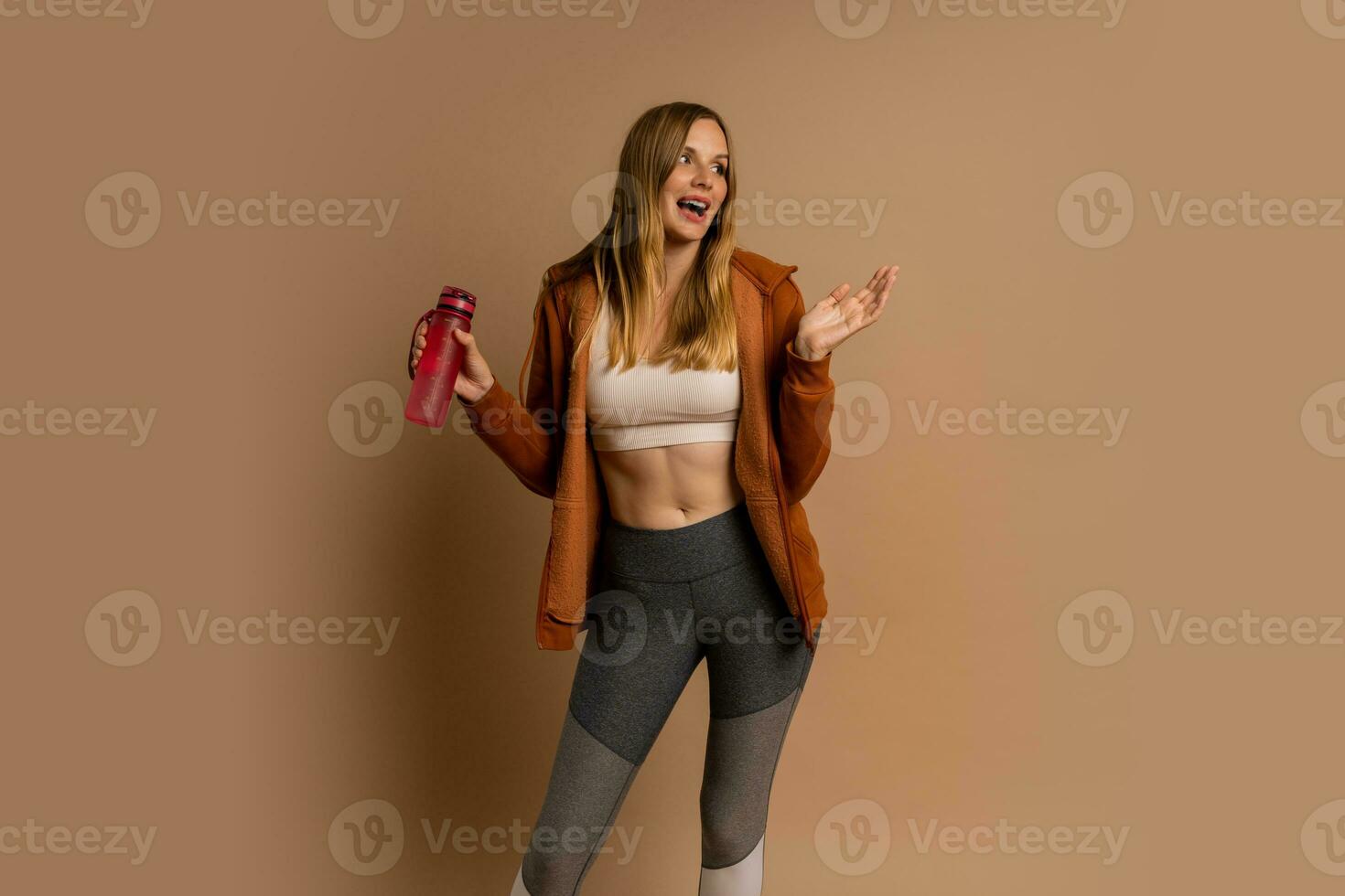 Pretty blond woman in sportive outfit  posing on beige background.  Holding bottle of water. photo