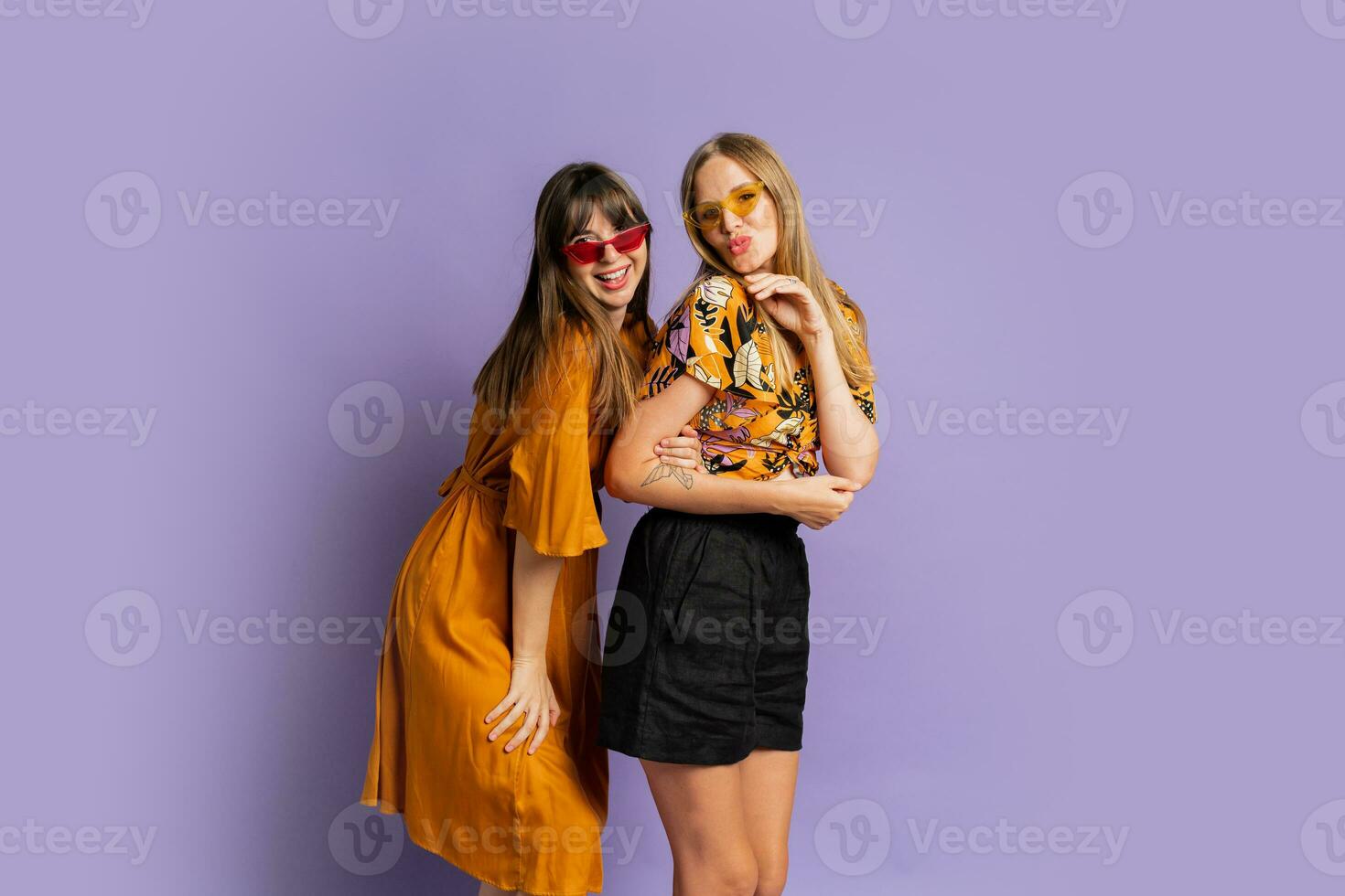 Two playful stylish women posing in studio over purple background. Friends dancing and having fun. photo