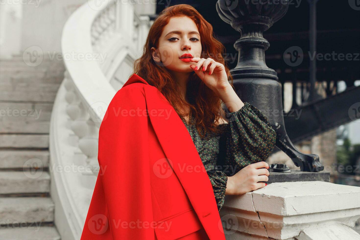 Lovely ginger female with perfect white skin looking forward. Wearing stylish red jacket and green silk dress. Wavy hairstyle. Paris fashion look. photo