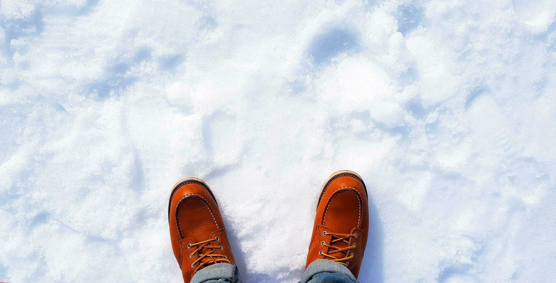 Top view or Flat lay of man's legs in blue jeans and wearing red or brown leather boots or snowshoes on snow with copy space on above. photo
