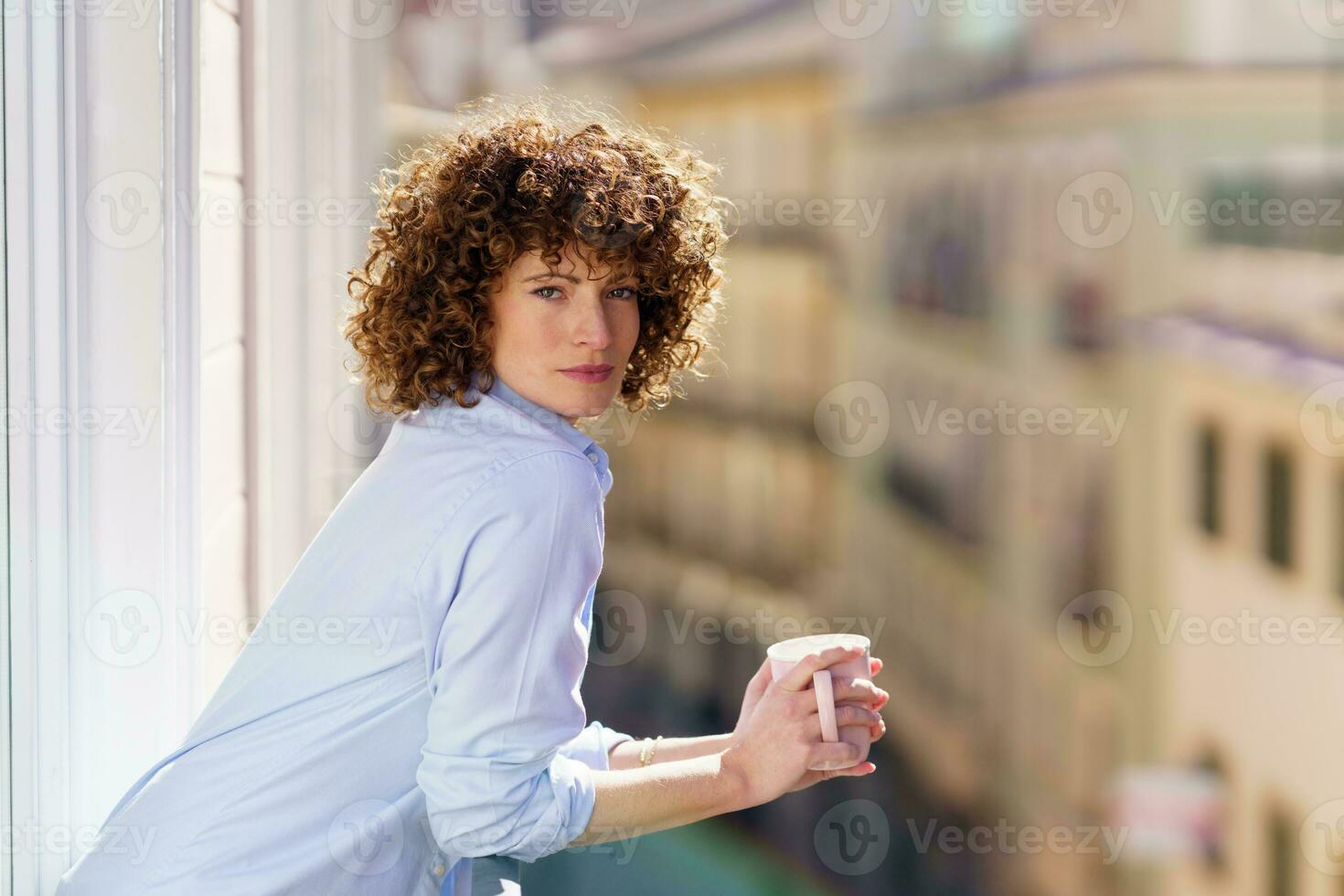 Curly haired female drinking coffee on balcony photo