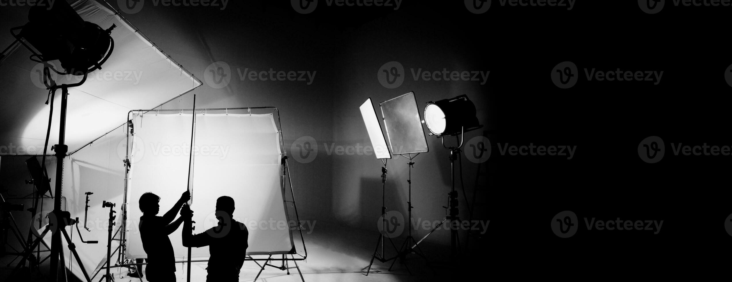 Silhouette of video production behind the scenes or B roll or making of TV commercial movie that film crew team lightman and cameraman working together with director in big studio with pro equipments photo