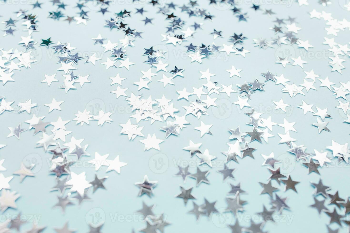 Trendy silver foil confetti stars on light blue background. Christmas festive abstract backround. Birthday party, New Year, Christmas celebration, holidays, winter and dreams concept. Selective focus photo