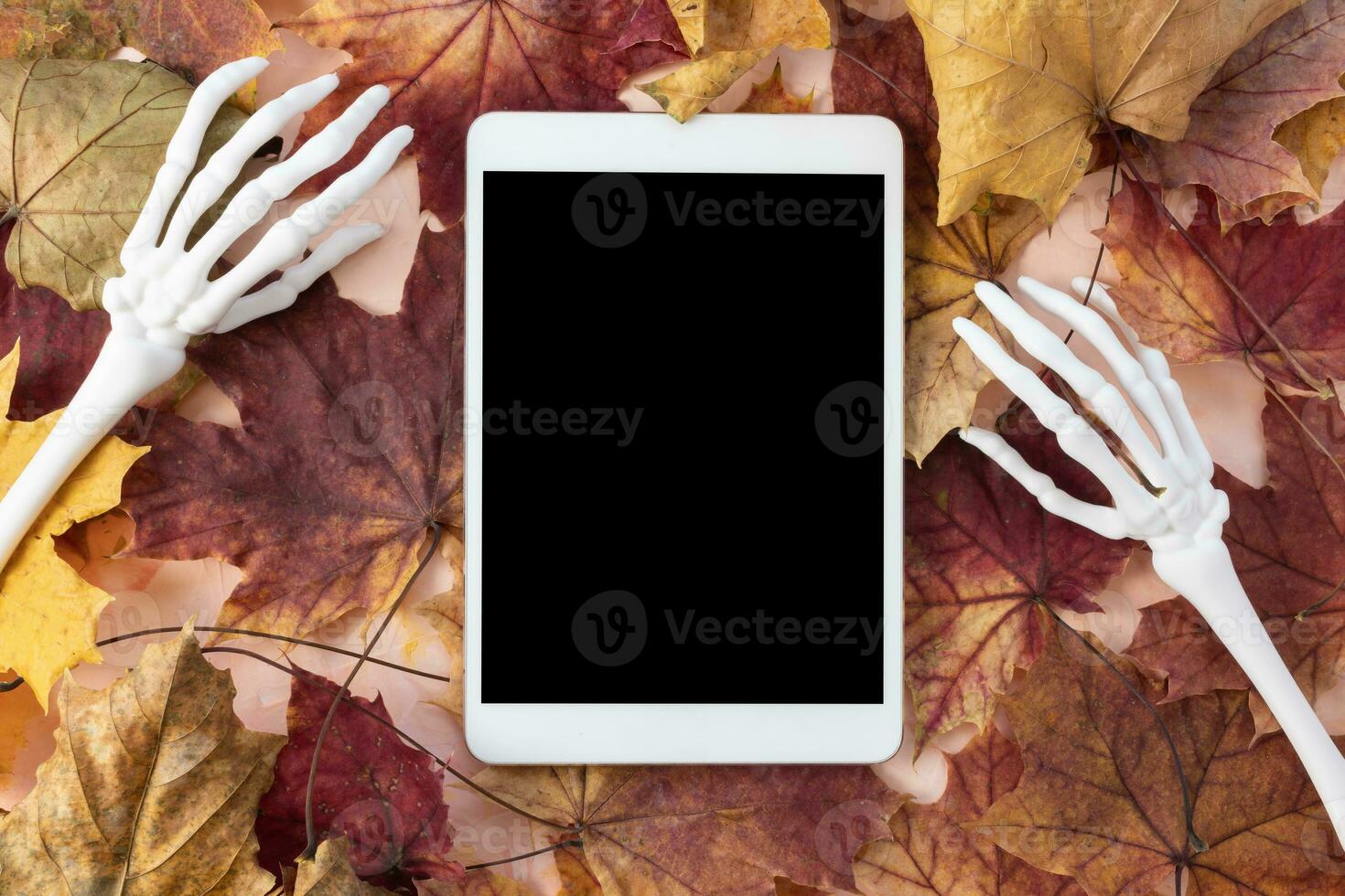 Digital tablet mockup with monster skeleton hands and autumn leaves background. Happy Halloween, online shopping, studying, sales mockup. Fall flat lay, top view. Internet application template photo