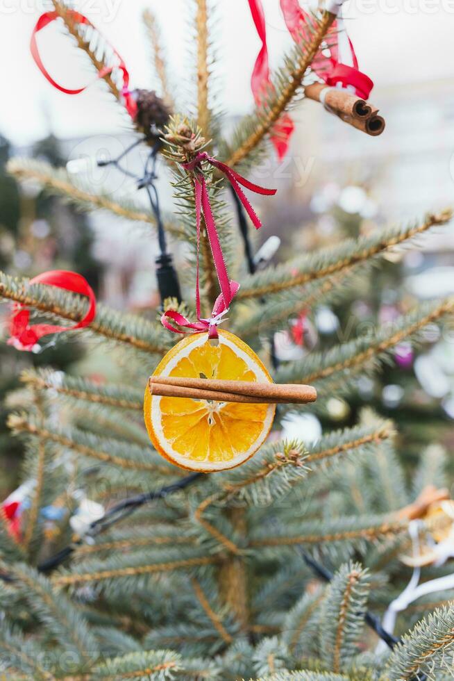 Natural decoration made of orange slices and Christmas spices on ribbon on Christmas tree. Diy Christmas decoration. Environment, recycle, reuse and zero waste concept. Selective focus photo