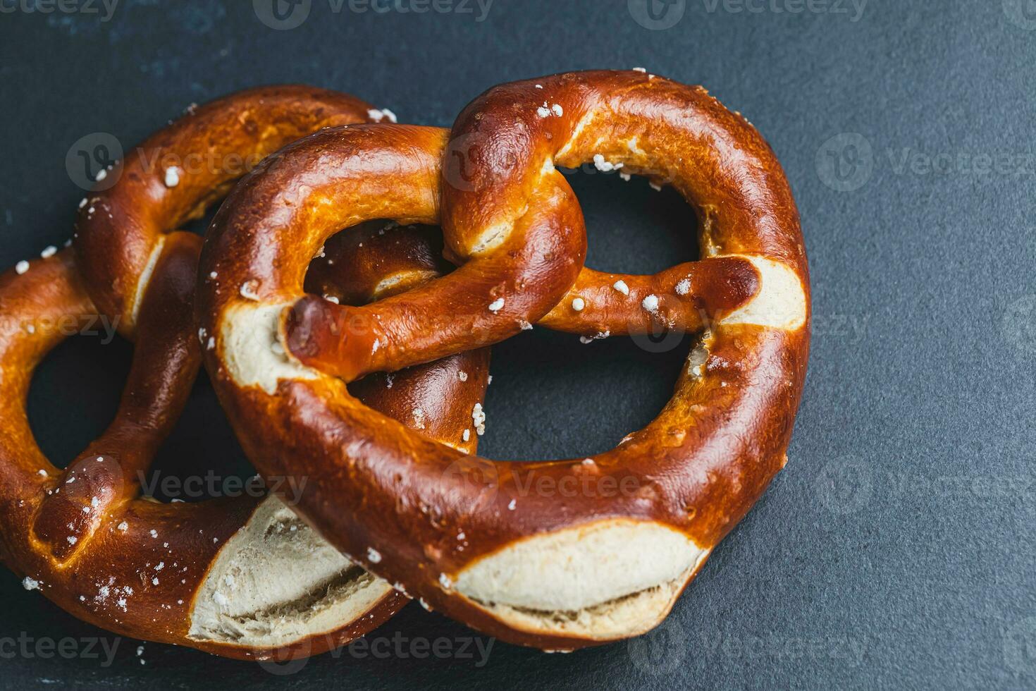 Two homemade freshly baked soft pretzels on black backround. Traditional Bavarian pretzel for Octoberfest. Top view, copy space photo