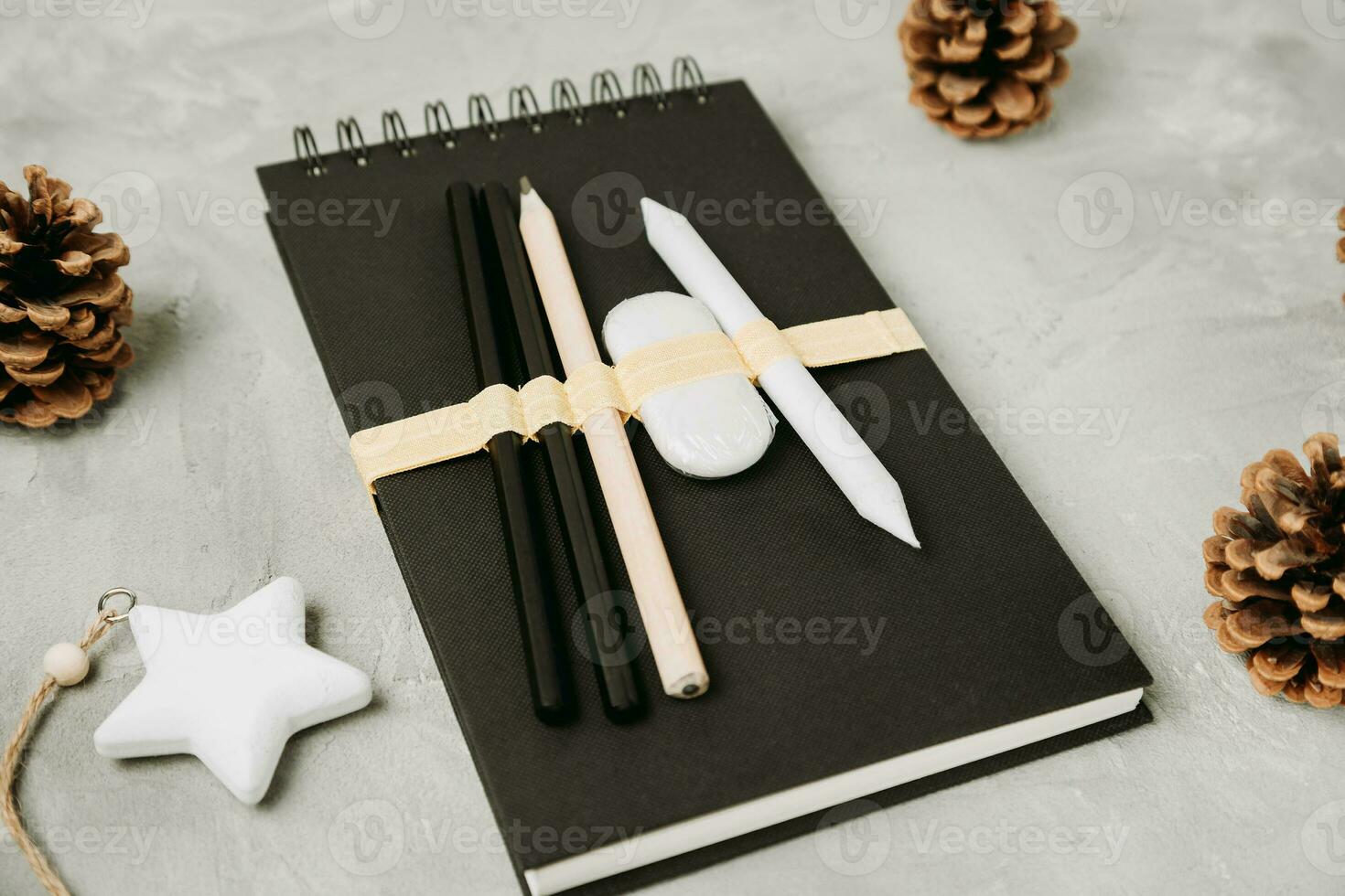 Sketchbook or notebook, pencils, eraser, pine cones, star on desk workspace, gray background. Christmas and New Year gifts for artist or children and lifestyle concept. Flat lay, top view, copy space photo