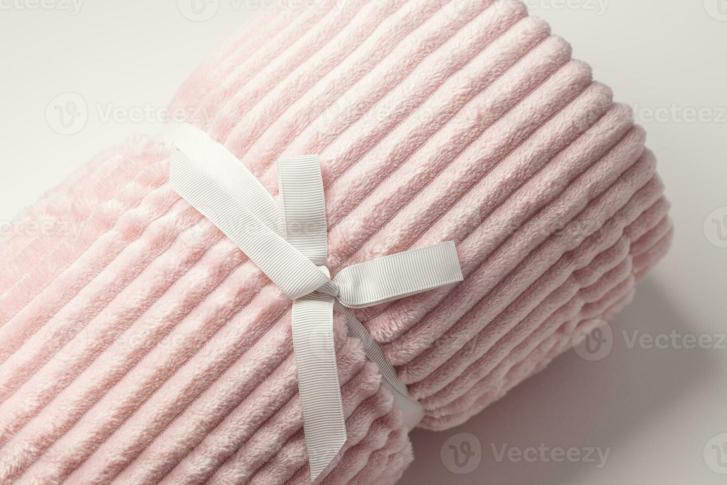 Soft pastel pink fleece throw fabric with lines roll up as gift with ribbon. White background, closeup, copy space photo