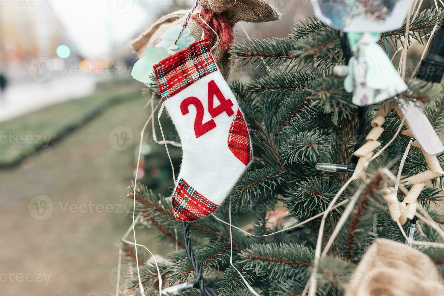 Handmade Christmas sock decoration with number or date 24 on a Christmas tree, outdoors. DIY for children. Environment, recycle, reuse, upcycling and zero waste concept. Selective focus, copy space photo