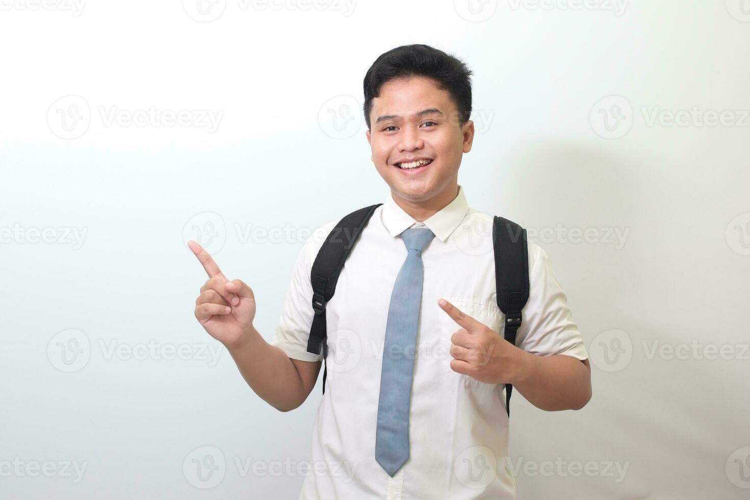 Indonesian senior high school student wearing white shirt uniform with gray tie showing product, pointing at something and smiling. Isolated image on white background photo