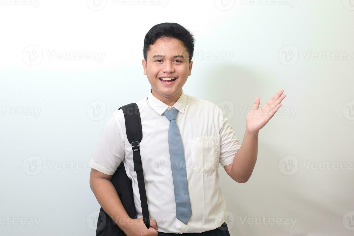 Indonesian senior high school student wearing white shirt uniform with gray tie showing product, pointing at something and smiling. Isolated image on white background photo