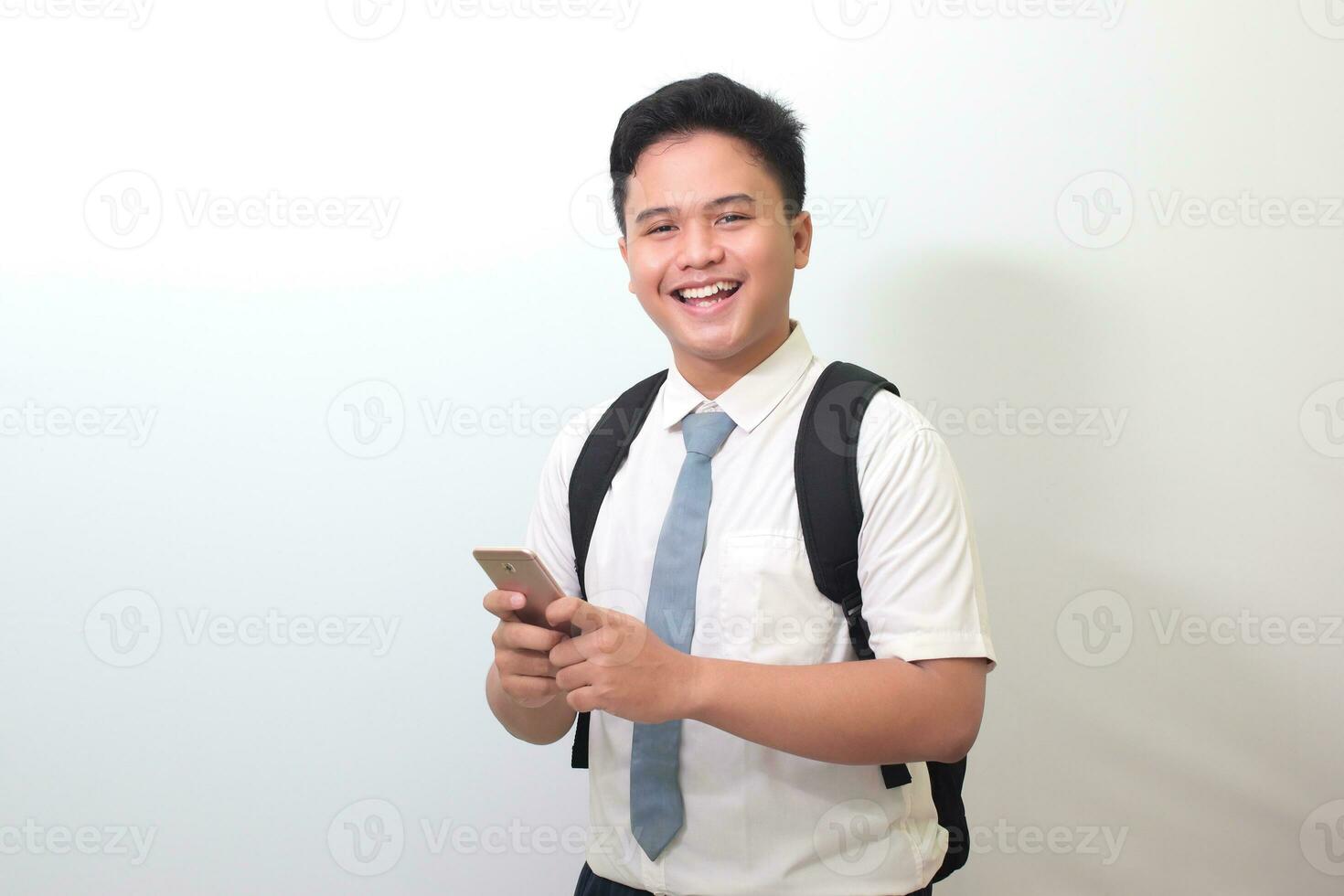 Indonesian senior high school student wearing white shirt uniform with gray tie showing shocked face expression while holding a mobile phone. Isolated image on white background photo