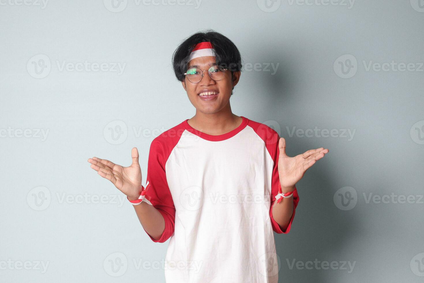 Portrait of attractive Asian man in t-shirt with red and white ribbon on head, pulling hands towards camera, inviting someone to come inside, welcoming gesture. Isolated image on gray background photo