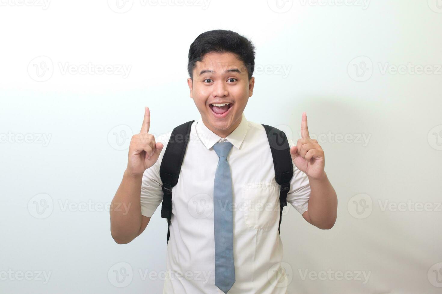 Indonesian senior high school student wearing white shirt uniform with gray tie showing product, pointing at something and smiling. Isolated image on white background photo