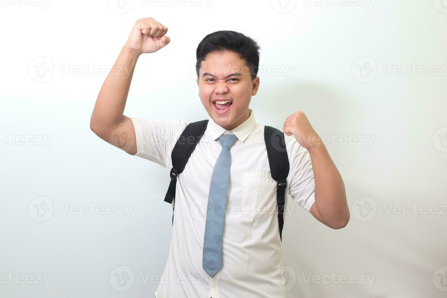 indonesio mayor alto colegio estudiante vistiendo blanco camisa uniforme con gris Corbata levantamiento su puño, celebrando éxito. victorioso un competencia concepto. aislado imagen en blanco antecedentes foto