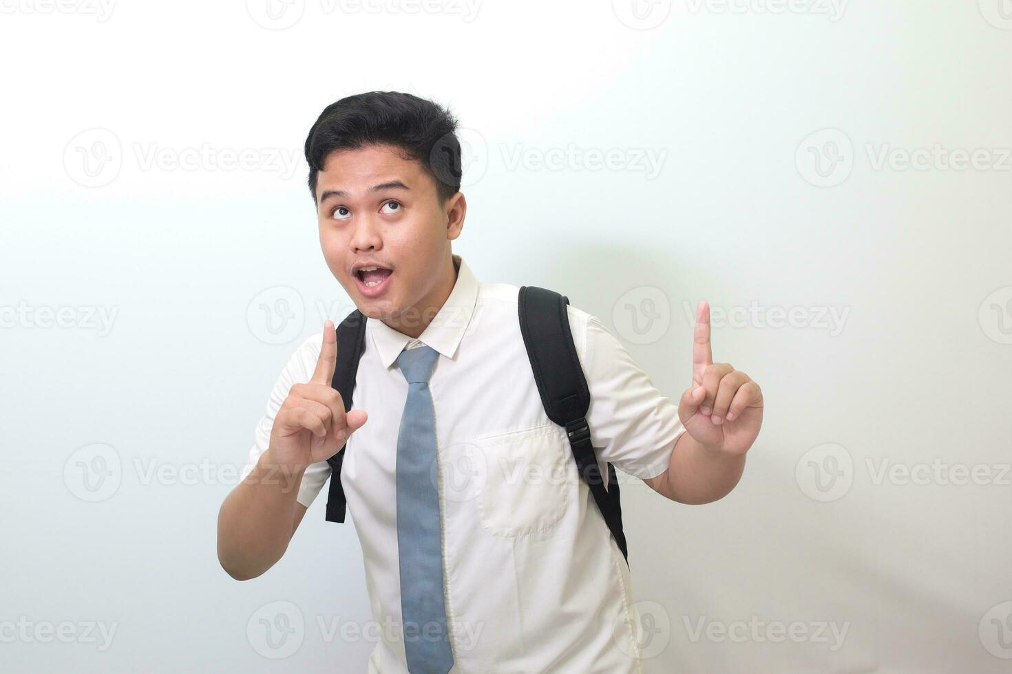 Indonesian senior high school student wearing white shirt uniform with gray tie showing product, pointing at something and smiling. Isolated image on white background photo