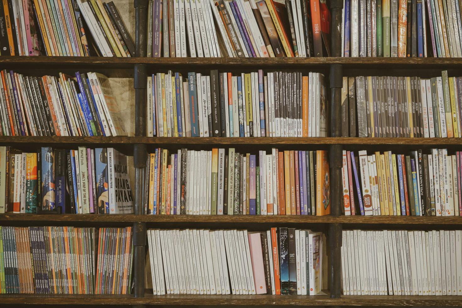 Industrial dark wooden bookshelves filled with social, fiction, self improvement and biography books in a public library or a bookseller shop. Yogyakarta, Indonesia - 08 28 2023 photo