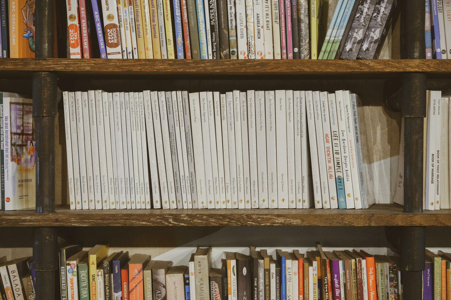 Industrial dark wooden bookshelves filled with social, fiction, self improvement and biography books in a public library or a bookseller shop. Yogyakarta, Indonesia - 08 28 2023 photo