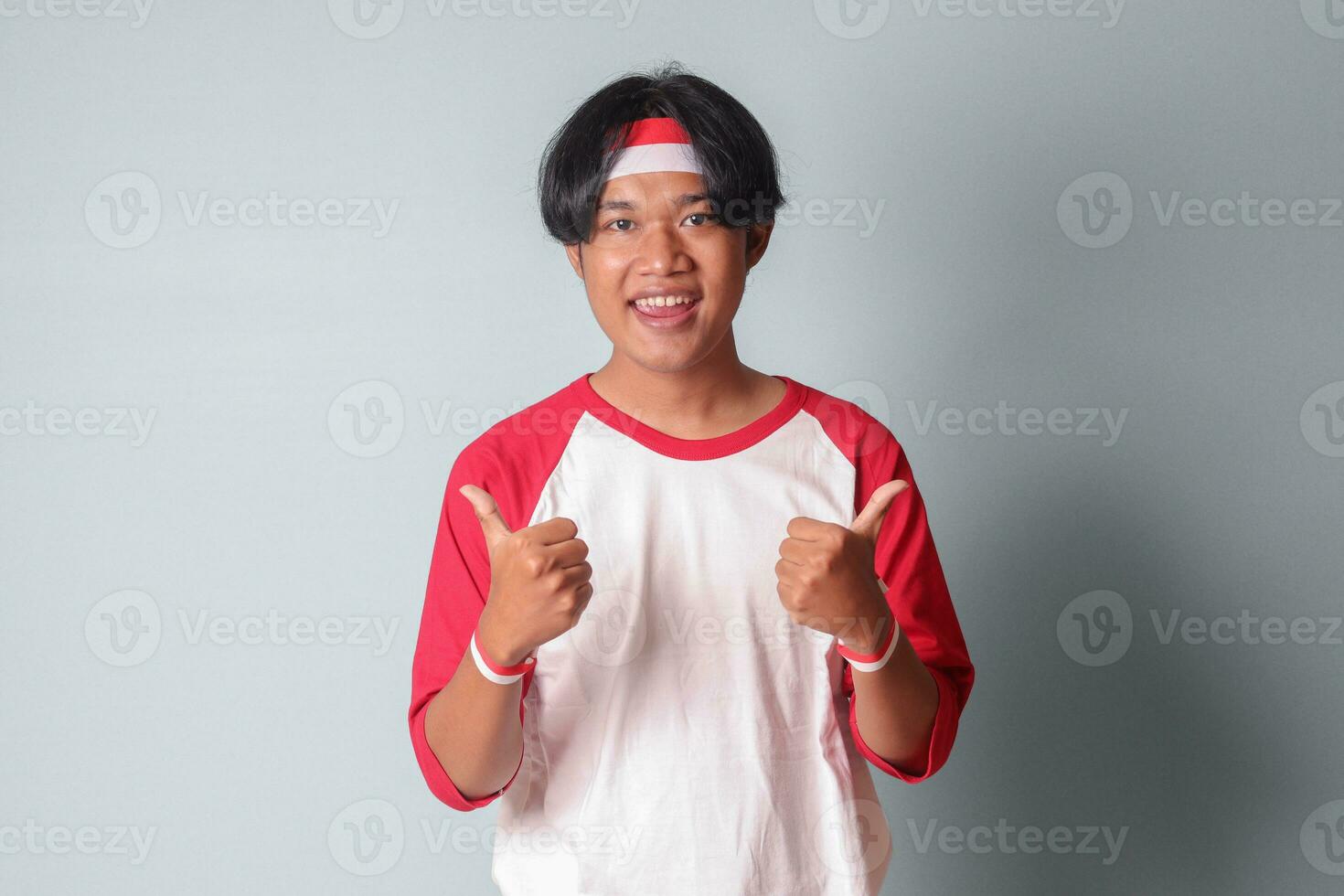 retrato de atractivo asiático hombre en camiseta con rojo y blanco cinta en cabeza, demostración bueno trabajo mano gesto con pulgares arriba. aislado imagen en gris antecedentes foto