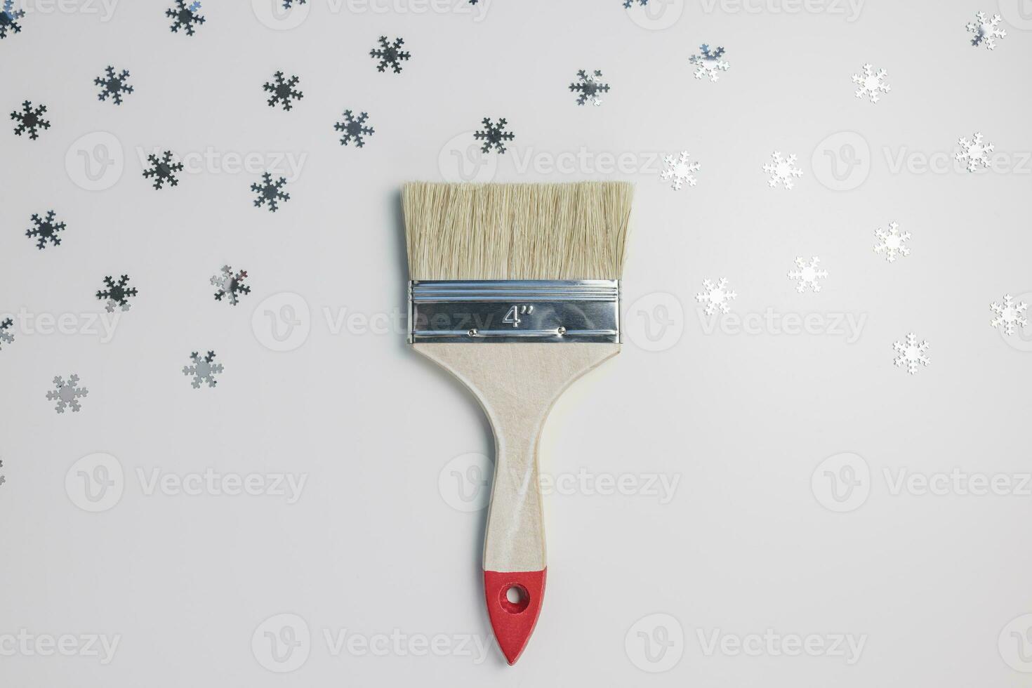 Wooden paint brush on gray with silver snowflakes background. Top view. Winter repairing concept photo