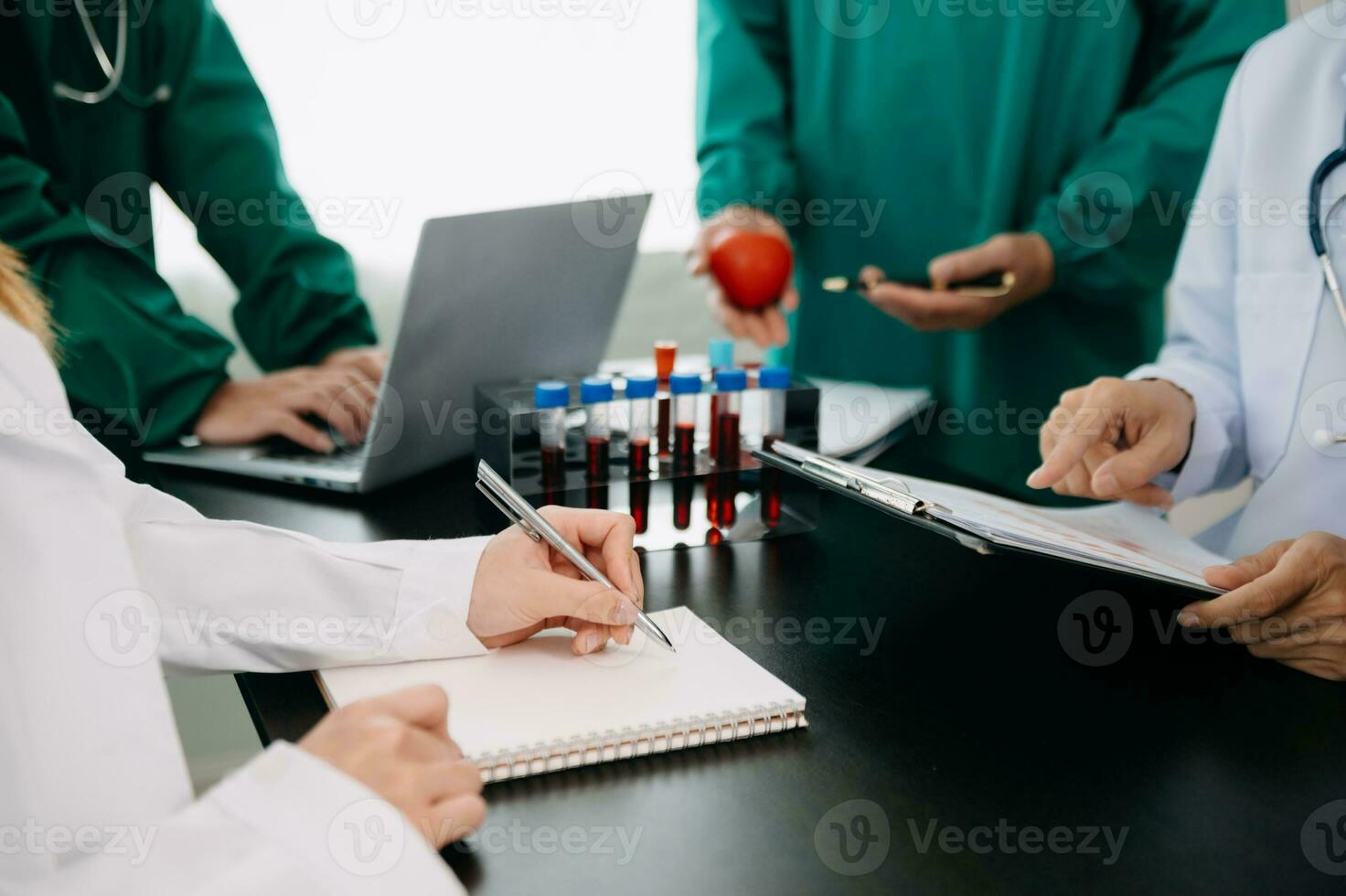 Medical team having a meeting with doctors in white lab coats and surgical scrubs seated at a table discussing a patients working online using computers in the medical industry photo