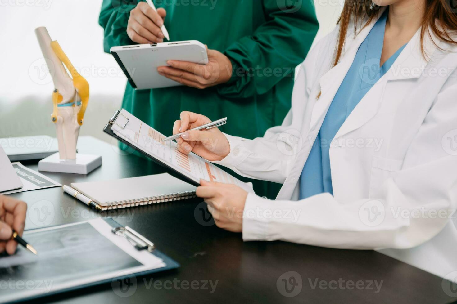 Medical team having a meeting with doctors in white lab coats and surgical scrubs seated at a table discussing a patients working online using computers in the medical industry photo