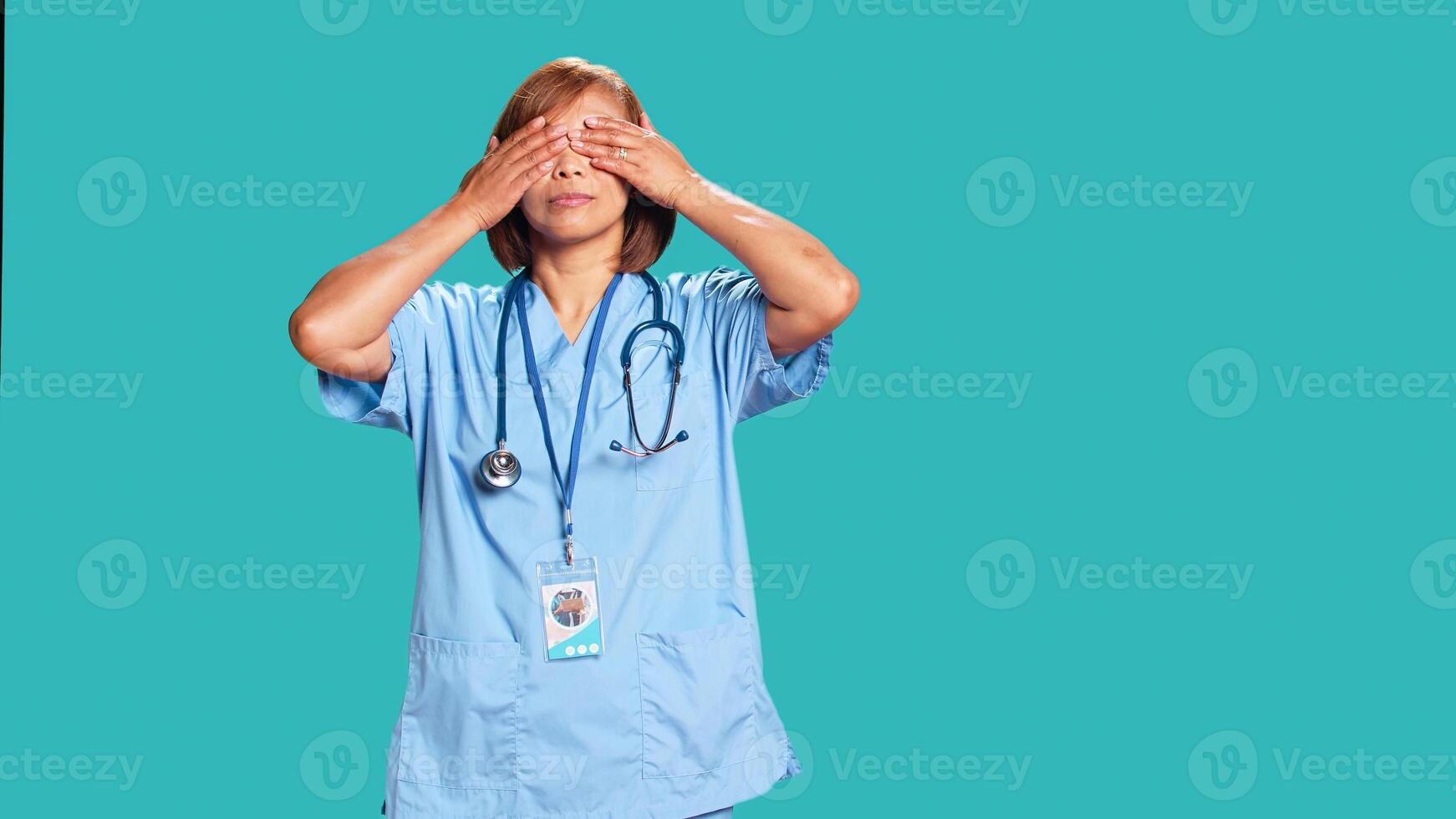 Healthcare expert covering eyes, ears and mouth with hands, imitating the three wise monkeys. Licensed nurse showing don t see, don t hear and don t speak concept, isolated over studio background photo