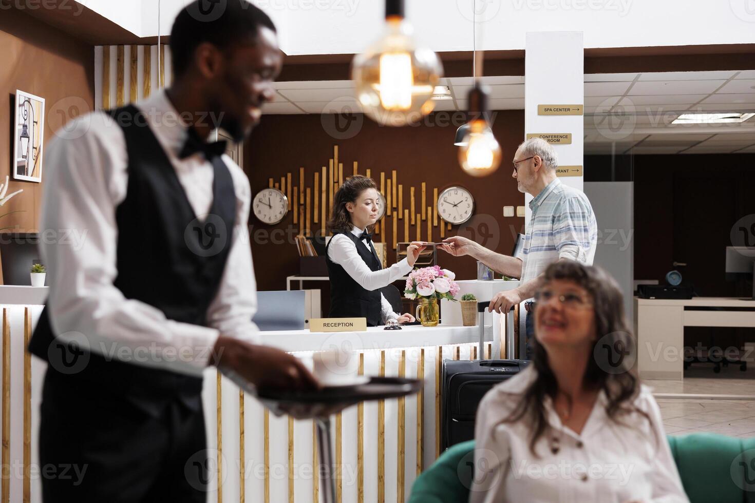 Arrival in hotel reception, elderly male customer checks in with receptionist assistance at front desk. Caucasian female concierge receives personal document from old man for smooth registration. photo
