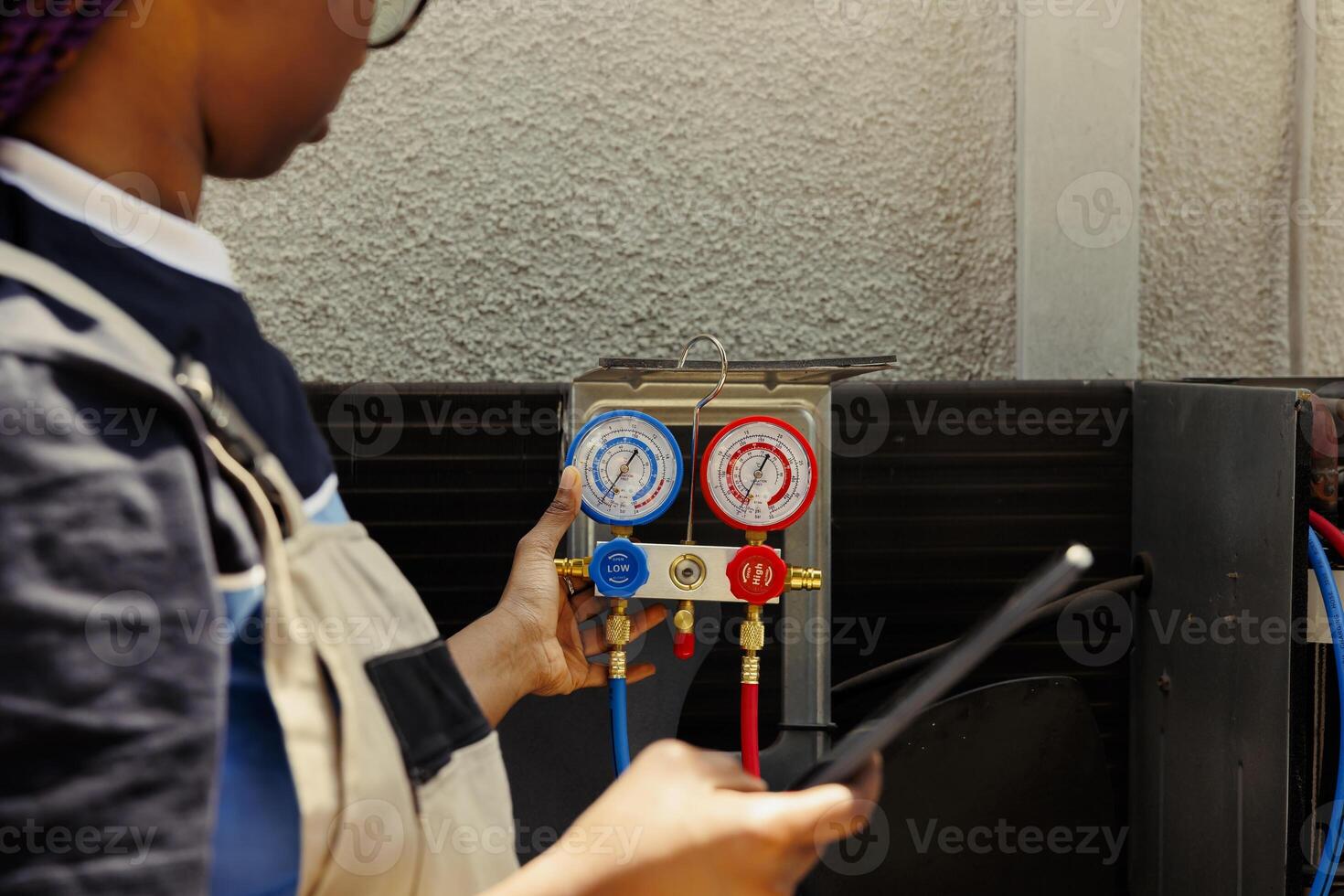 Proficient african american worker hired by home owner to restore cooling capacity of condenser by inspecting system for leaks and recharging it with new refrigerant to prevent damage to evaporator photo