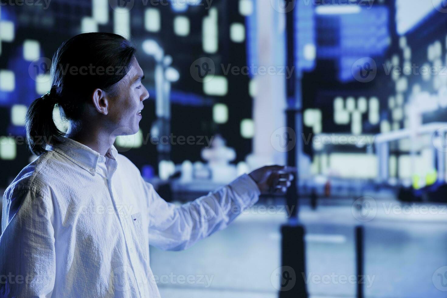 Relaxed asian man wandering around city streets at night, looking around to surrounding skyscrapers in metropolitan urban setting. Businessman leaving work, taking a walk outside empty town photo