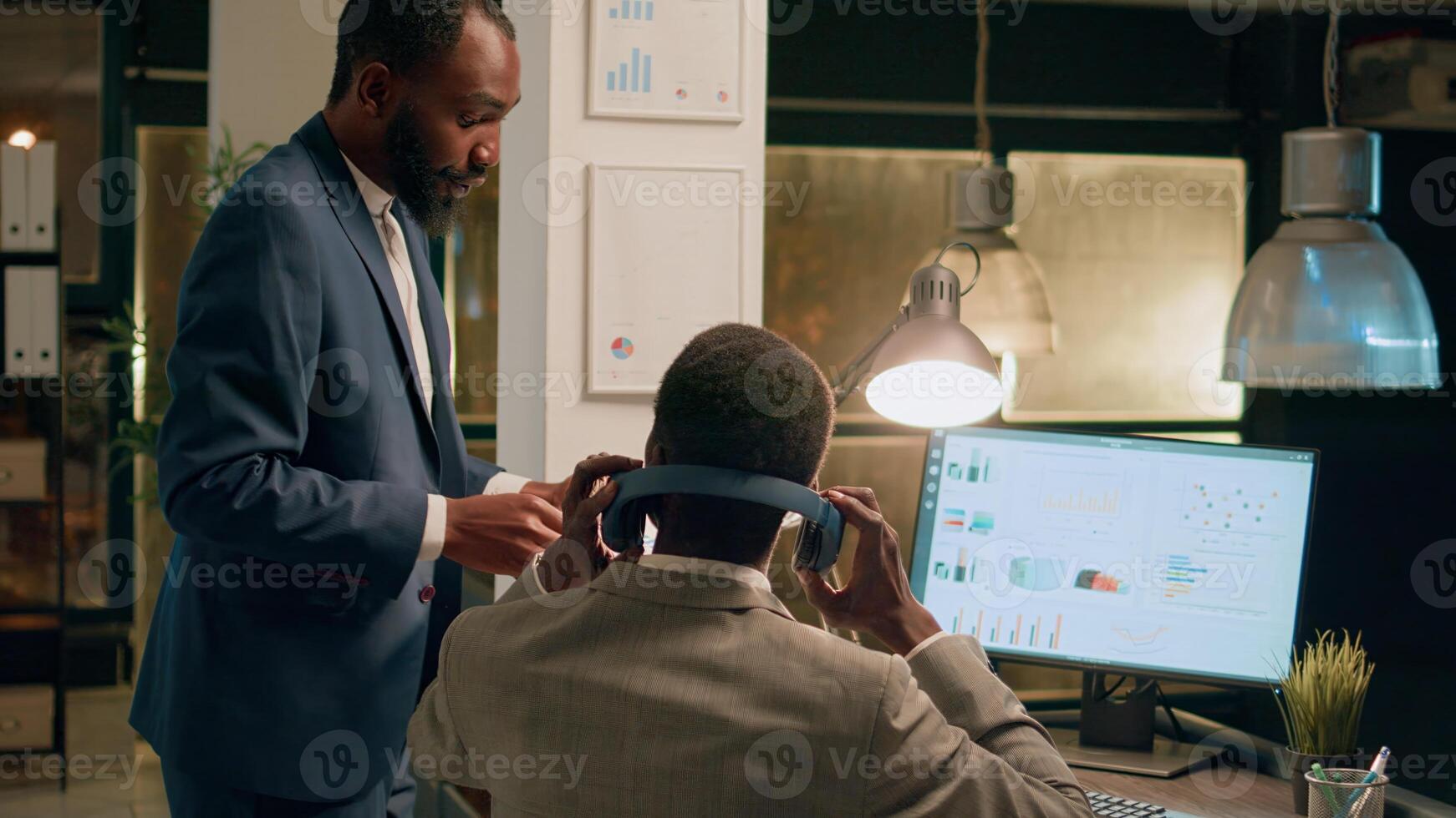 Business manager interrupting worker listening to music while imputing data on computer to show him project results. Supervisor showing employee financial figures in office during nightshift photo