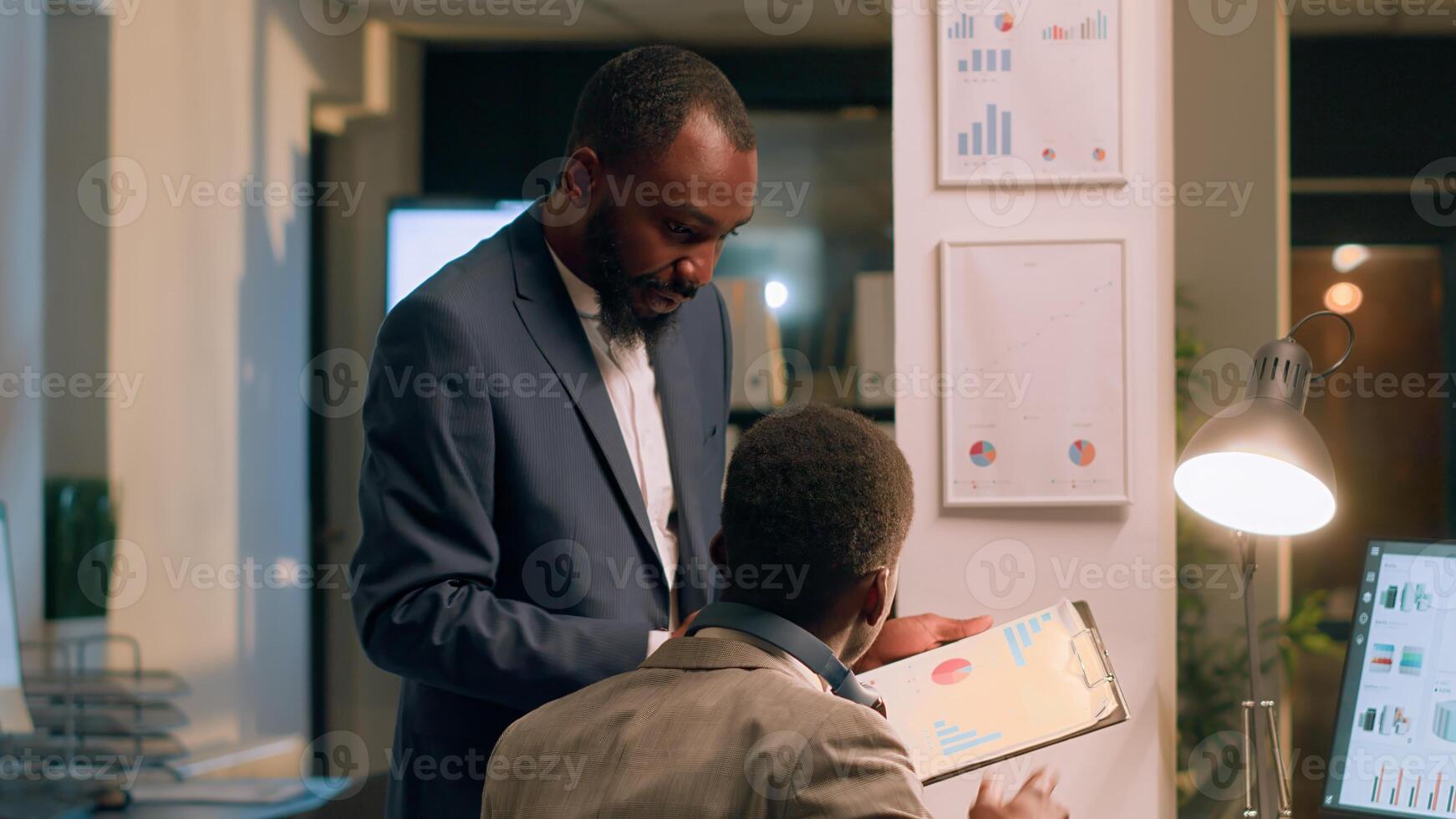 Office manager interrupting distracted worker listening to music while checking statistical graphs to show him mistake he needs to fix. Supervisor analyzing project performance with employee photo
