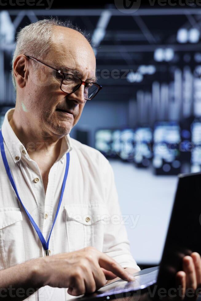 Computer scientist inspects supercomputers in data center, ensuring smooth performance. Knowledgeable specialist in server room monitoring energy consumption across units components using laptop photo