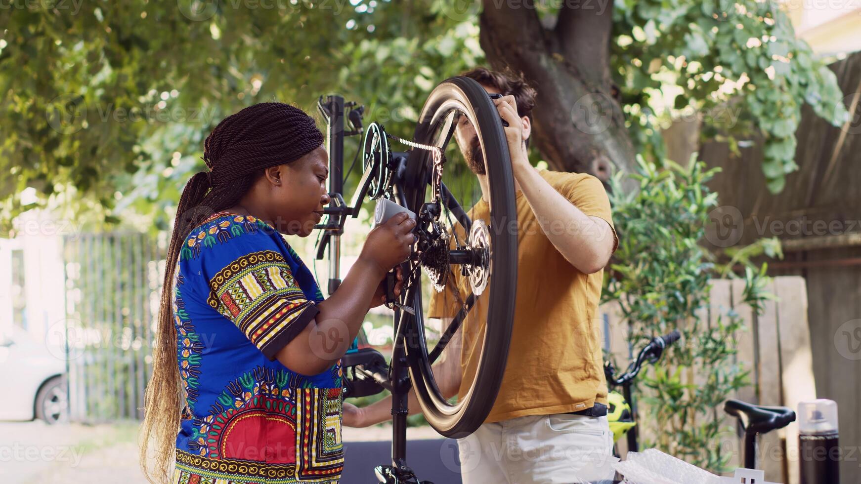 Active motivated interracial couple outside adjusting bike wheel with professional equipment. Young black woman grabbing specialized tools to assist caucasian man in fixing bicycle. photo