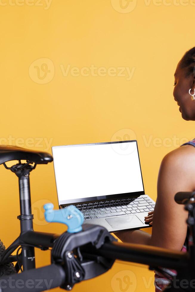 Closeup shot of laptop with isolated chromakey template carried by african american female. In front of yellow background, black person is holding wireless computer displaying blank whitescreen. photo