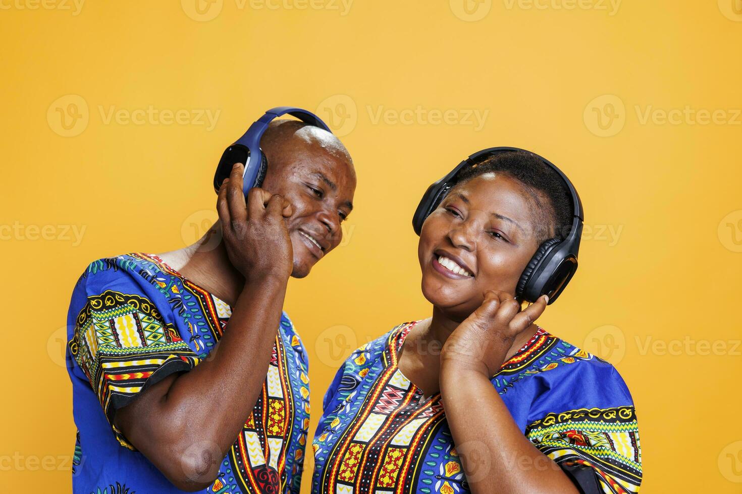 Smiling african american romantic couple wearing ethnic clothes enjoying music together in wireless headphones. Man and woman with joyful expression listening to song in studio photo