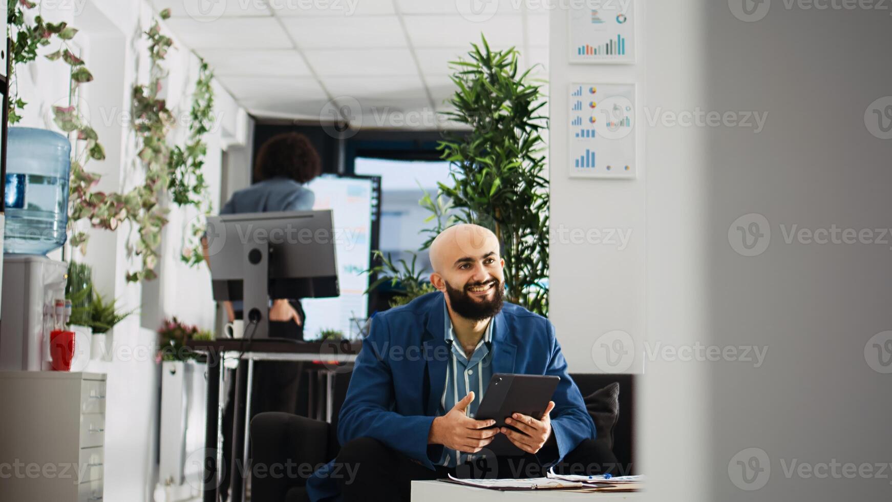 Company employee researching analytics on tablet, using past marketing statistics reports. Middle eastern man working with official documents to create small business development plan. photo