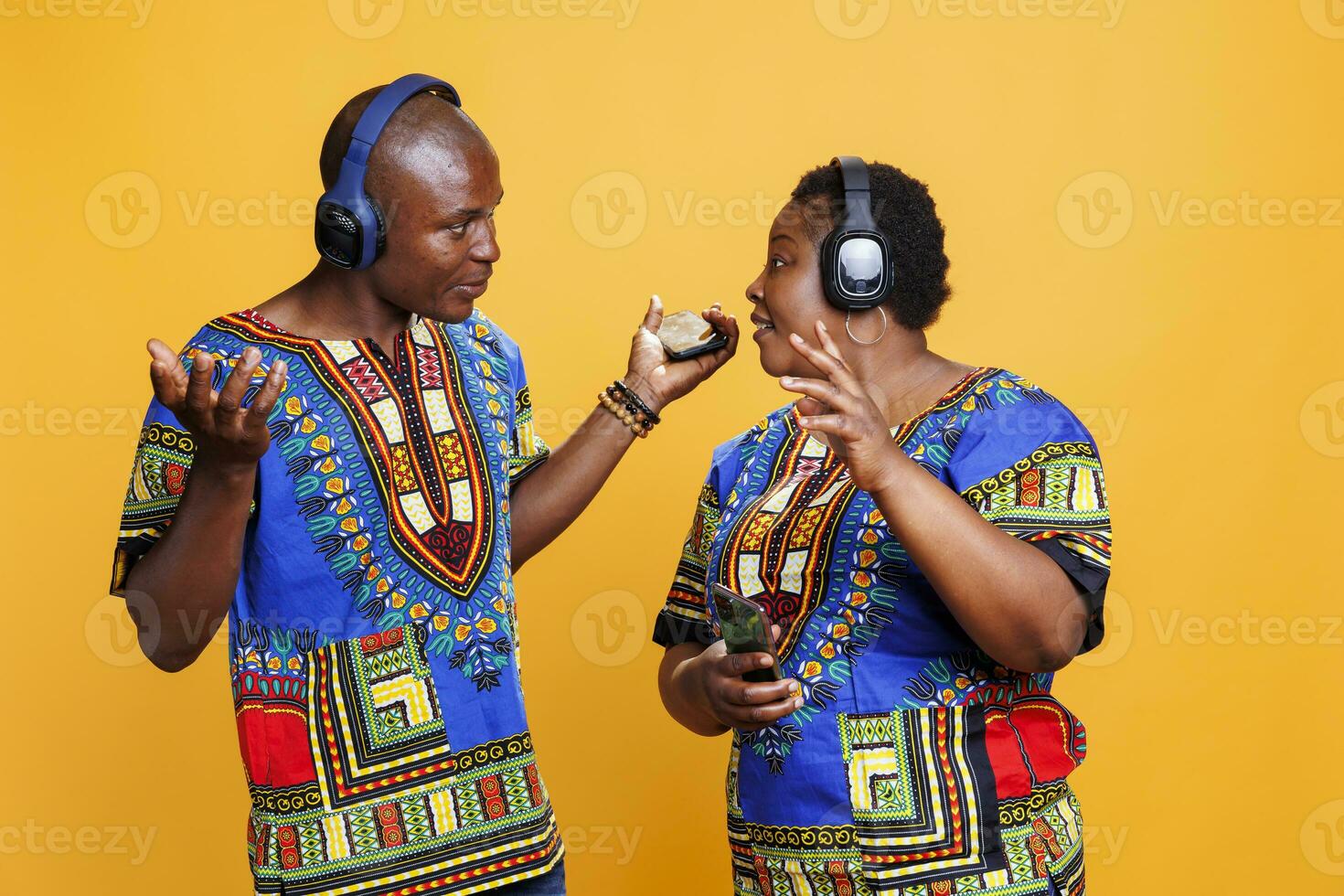 African american couple in wireless headphones listening to music and discussing sound. Man and woman wearing earphones enjoying song and talking while holding smartphone photo