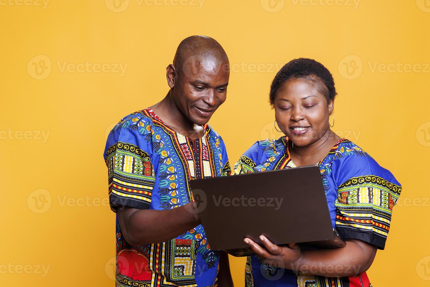 Smiling african american man and woman couple working on laptop together. Wife and husband with joyful expression holding portable computer and surfing internet on studio background photo