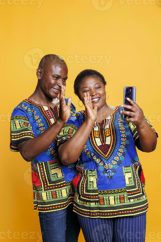 Smiling man and woman greeting and waving hello while having online call on smartphone together. Cheerful happy couple holding mobile phone and speaking in remote videocall photo