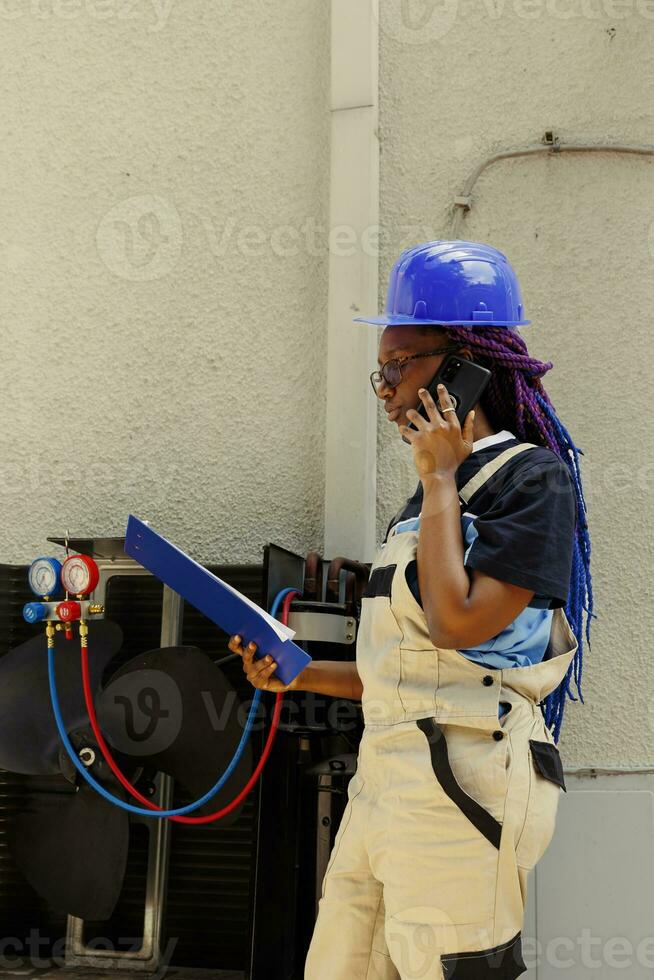Precise technician apprentice offering informations about air conditioner needing to be replaced to master over the phone. Engineer checking maintenance plan after fixing faulty compressor photo