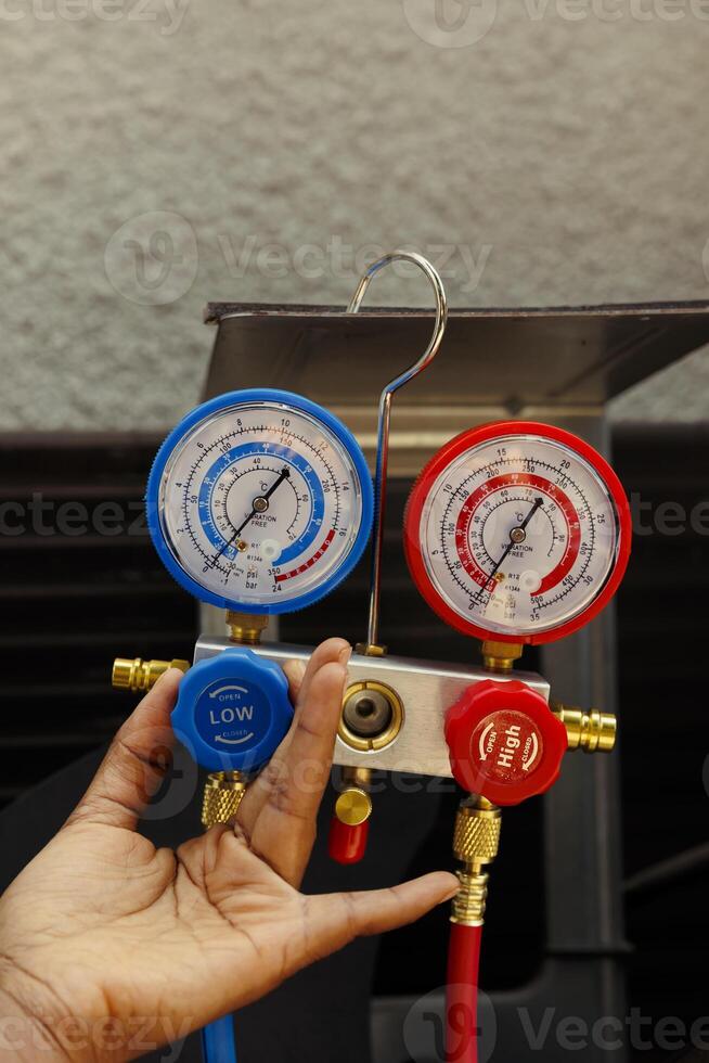 Close up of ac gauges vacuum pump able to find busted expansion valve, freon not circulating properly and other issues. Seasoned wireman using manifold indicators to read condenser pressure levels photo