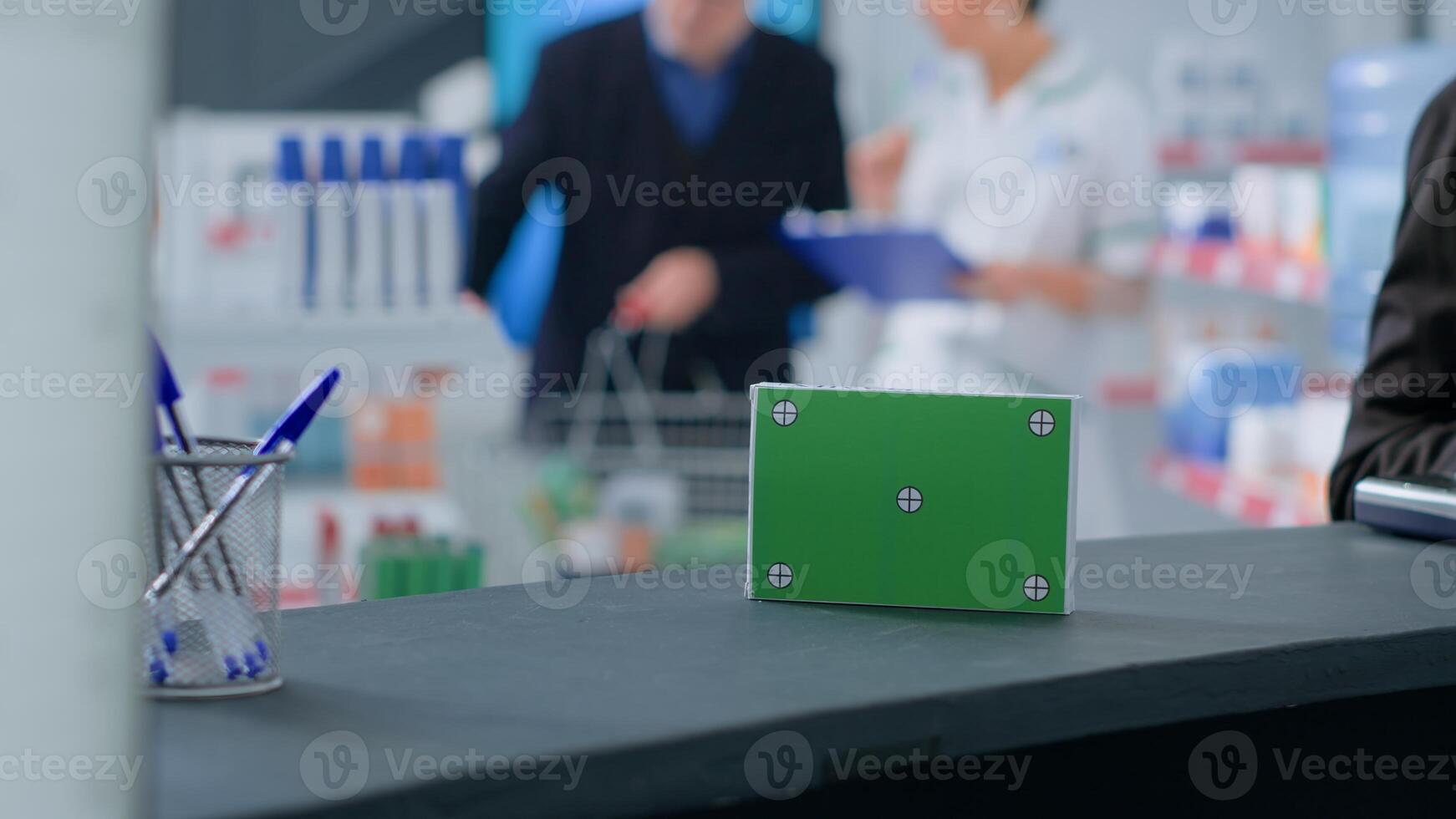 Close up shot of isolated packaged pharmaceutical product standing on dispensary counter, with client in background purchasing sickness treatment medication from experienced druggist photo