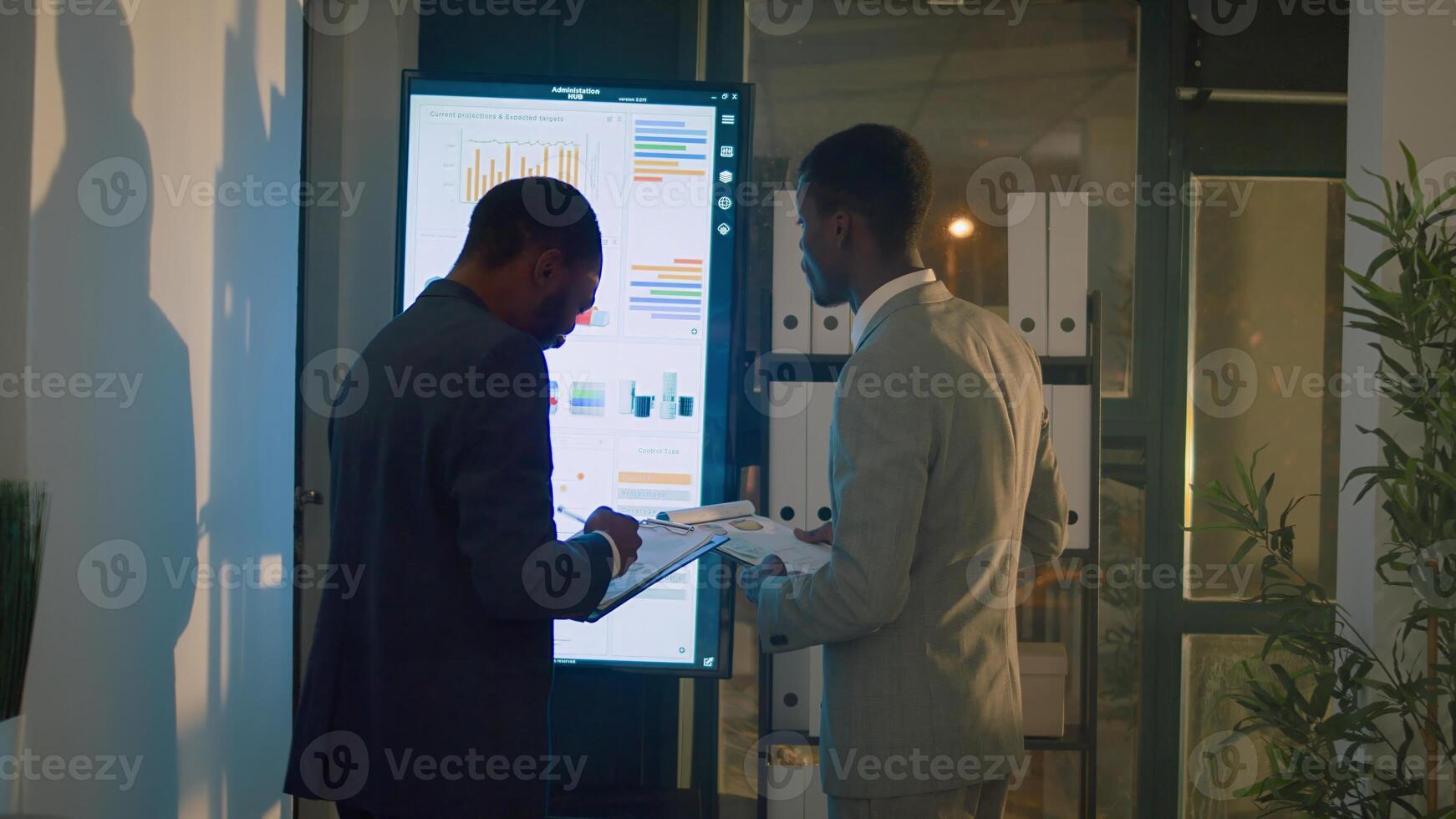 Manager annoyed by lack of project progress in office during nightshift, checking financial charts with employee. Management executive frustrated by slow worker struggling with audit task photo