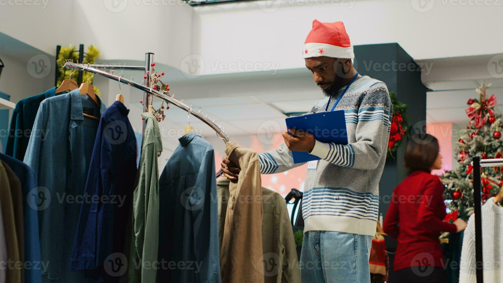 Retail manager browsing through clothing racks in Christmas decorated fashion store, crosschecking price tags with clipboard list. Supervisor inspecting stylish blazers, looking for defects photo